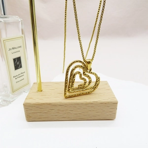 Detailed view of layered 18K gold heart pendant necklace on a wooden jewelry display stand