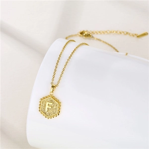 Detailed close-up of a golden hexagonal pendant with a bead border and letter F engraving