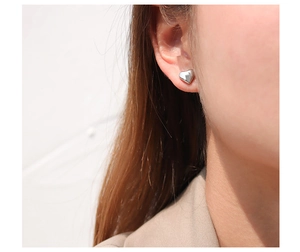 Detailed close-up of a minimalist silver heart stud earring worn on a female ear model