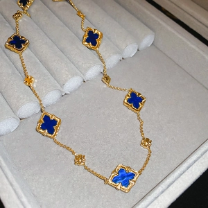 Close-up of golden necklace with blue clover charms on a luxury gray velvet tray