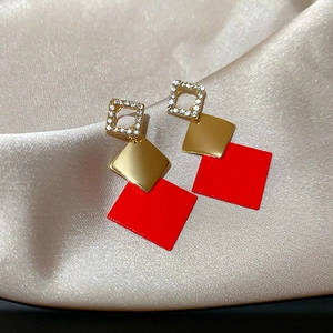 Detailed macro of geometric drop earrings with red accents on champagne silk