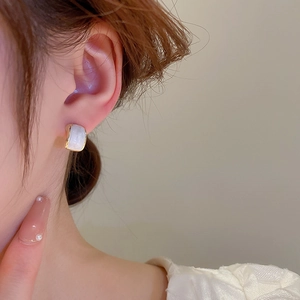 Detail of elegant gold geometric earring with white resin inlay worn on ear