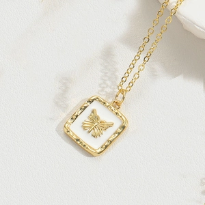 Close-up of golden necklace featuring a white square pendant with a detailed gold butterfly