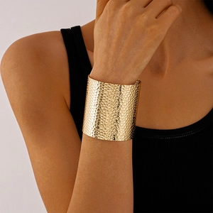 Detail of a wide gold cuff bracelet featuring a textured hammered metal finish on a wrist