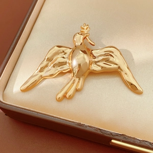 Close-up of a polished gold bird brooch with olive branch on beige satin inside a luxury box