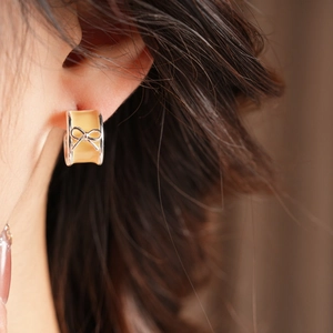 Detail of cream yellow enamel hoop earring with silver metal bow on a model ear