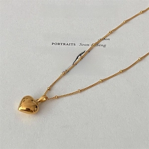 Close-up of golden heart pendant on a beaded chain placed over minimalist art paper