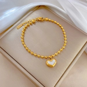 Close-up of titanium steel gold beaded bracelet with a white mother-of-pearl heart charm
