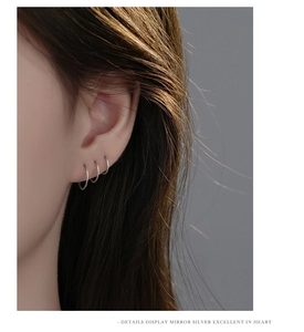 Close-up of three minimalist silver hoop earrings layered on a model's ear