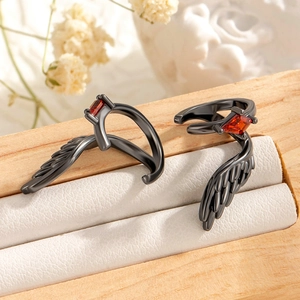 Gothic gun black angel wing rings with red gemstones on a wooden jewelry display case