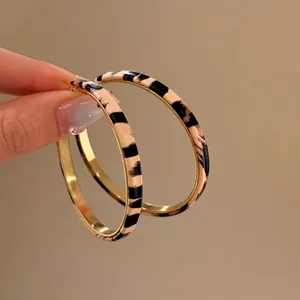 Stylish gold hoop earrings with animal print texture held against a solid background