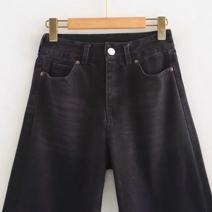Loose fit washed black high-waisted denim jeans displayed on a wooden hanger against a wall