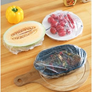 Elastic disposable food covers on melon and bowls over a wooden kitchen table