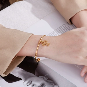 Close-up of golden stainless steel cross charm bracelet worn on wrist with beige suit