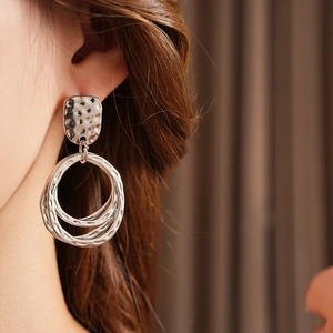 Close-up of silver geometric hoop earrings with hammered texture and hollow squares