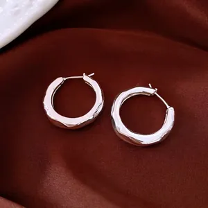 Polished silver hoops with irregular liquid metal texture on dark silk fabric