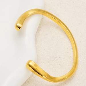 Close-up of minimalist irregular gold bracelet on white ceramic plate with metal texture