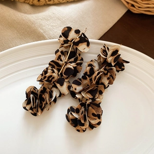 Macro shot of leopard print fabric flower tassel earrings displayed on a ceramic tray
