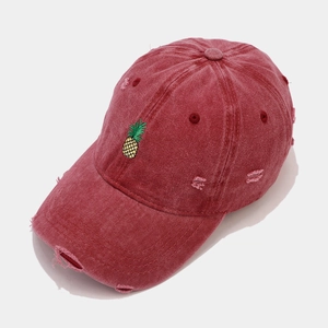 Close-up of distressed red cotton baseball cap featuring pineapple embroidery and worn edges