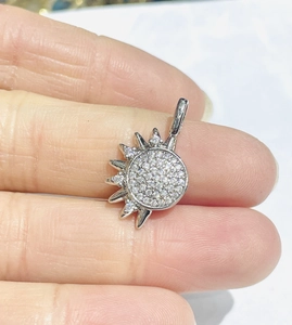 Detailed macro view of a silver sun pendant with cubic zirconia inlay held on a finger