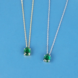 Elegant 18K gold and silver pear-shaped emerald zircon necklaces on a clean blue surface