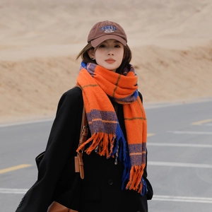 Plaid scarf with orange and blue tassels and a brown baseball cap in a desert road setting