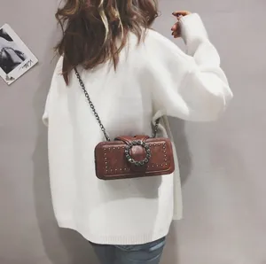 Detail of a brown leather crossbody bag with metal rivets and a large crystal buckle