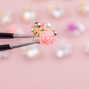 Macro shot of 3D pink resin rose nail charms with pearls and gold beads on tweezers