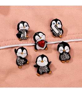 Collection of cute enamel penguin brooches with rhinestones on pink fabric background