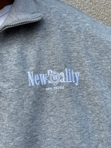 Detail of half-zip grey sweatshirt showing premium embroidery and metal zipper hardware