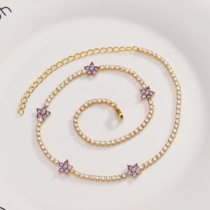 Macro detail of gold flower necklace with purple zircon petals on white plate
