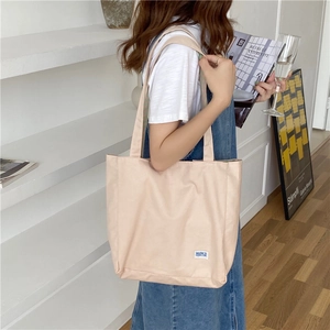Detalle del bolso tote minimalista de lona beige con etiqueta lateral y correa de hombro