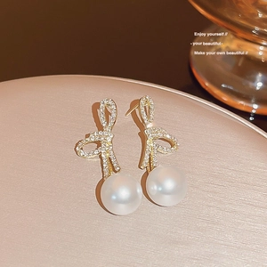 Detailed macro shot of golden bow earrings with sparkling pavé zircons and white pearls