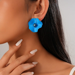 Close-up of a model wearing a large blue matte flower stud earring with a central gem