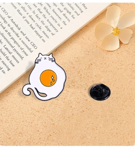 Detail of creative cat enamel pin with fried egg design and black butterfly clutch back