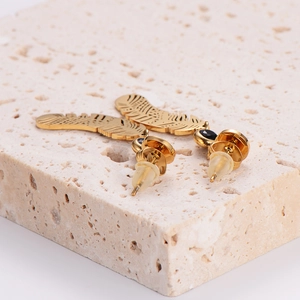 Minimalist gold feather stud earrings with black gemstone inlays on a stone base