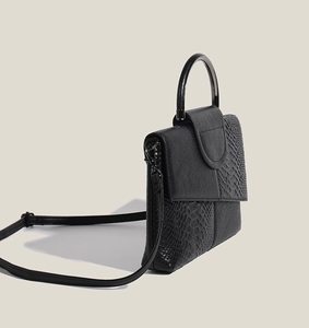 Detailed close-up of a black handbag featuring mixed smooth and crocodile textures with handle