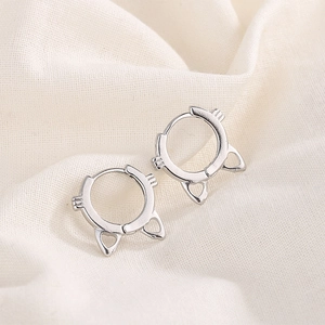 Macro detail of silver cat ear hoop earrings with engraved whiskers on white fabric