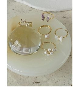Detail of golden butterfly rings with white pearls and purple enamel on a jade base