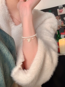 Primer plano de la pulsera de doble capa con perlas y dije de camelia en la muñeca