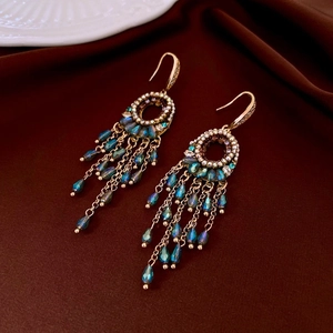 Detail of elegant gold tassel earrings with blue crystals on deep red velvet background