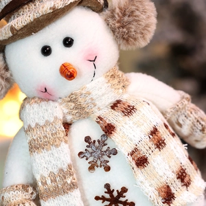 Dettaglio di un pupazzo di neve in peluche con sciarpa a quadri marroni e fiocco di legno