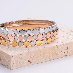 Stack of elegant stainless steel heart bracelets with white shell inlay on stone base