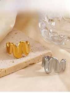 Detailed view of wave-shaped rings in gold and silver finish on textured stone surface