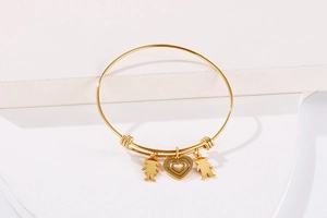Detail of adjustable gold heart bracelet with boy and girl charms on a white stand