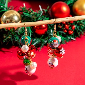 Detail of beaded Santa Claus and snowflake earrings hanging on a branch in festive setting