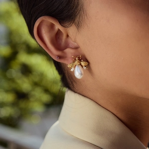 Macro shot of gold bee earring featuring clear crystals and white teardrop pearl drop