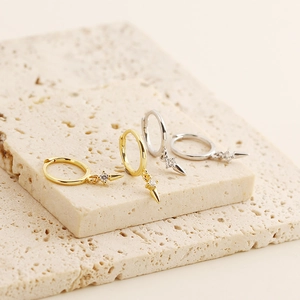 Detail of silver and gold huggie earrings with sparkling cross star charms on stone