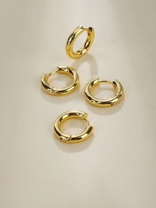 Detail of four gold-plated minimalist hoop earrings set on a warm beige background