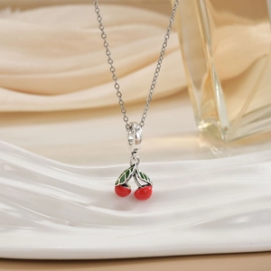 Detail of silver cherry necklace with red enamel pendants on white display stand